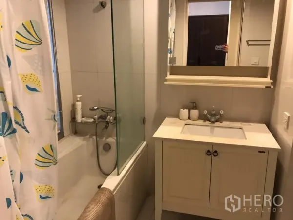 Condominium for rent in Pathum Wan, Bangkok - Bathroom with bathtub and glass shower screen, white vanity and mirrored cabinet.