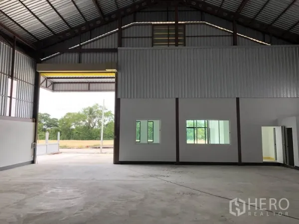 Factory for rent or sale in Sai Noi, Nonthaburi - High-ceiling production hall with a wide roller door, concrete floor and internal office windows.
