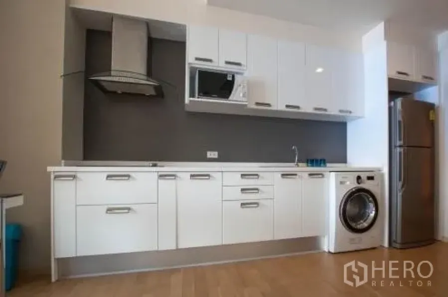 Condominium for rent or sale in Watthana, Bangkok - Modern white linear kitchen with built-in cabinets, hood, microwave, sink, washing machine and stainless refrigerator.