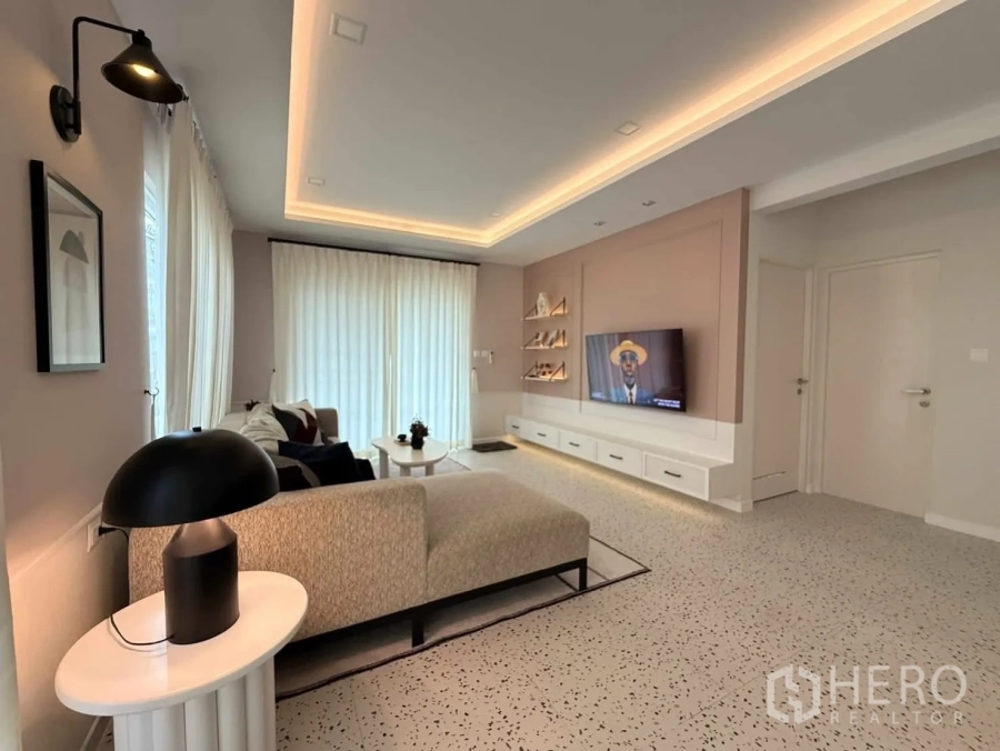 Detached House for rent in Bang Phli, Samut Prakan - Living room with cove lighting, L-shaped sofa, TV feature wall and low cabinets.