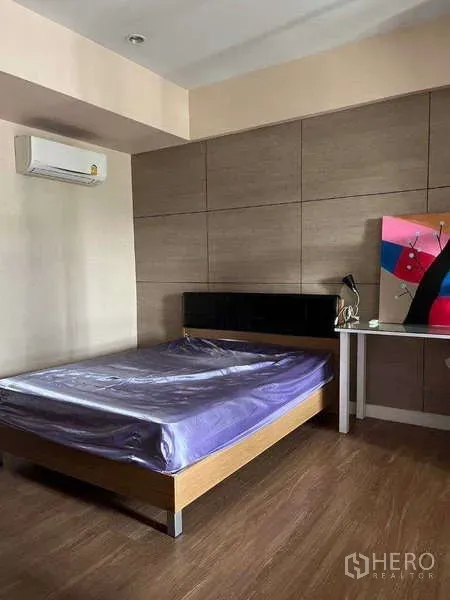 Townhouse for rent in Khlong Toei, Bangkok - Bedroom with wooden flooring, paneled accent wall, air conditioner, and bed beside a small desk.