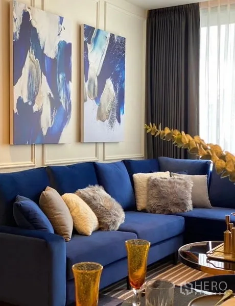 Condominium for rent - Blue L‑shaped sofa with textured cushions under abstract blue paintings and sheer curtains.