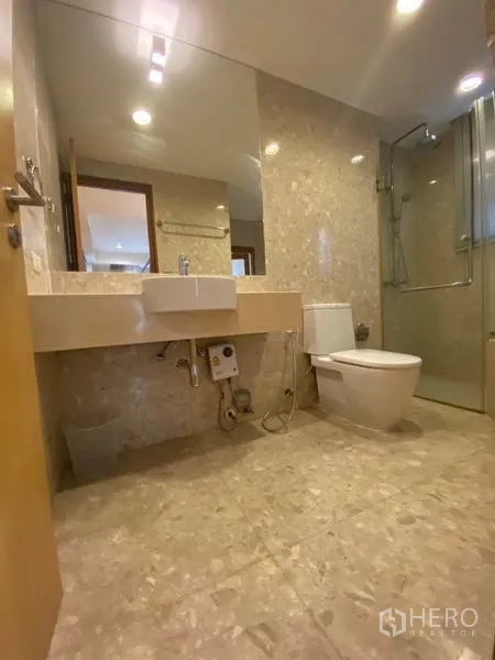 Condominium for rent in Watthana, Bangkok - Second bathroom with vanity, toilet, and glass-enclosed shower over stone-effect tiles.