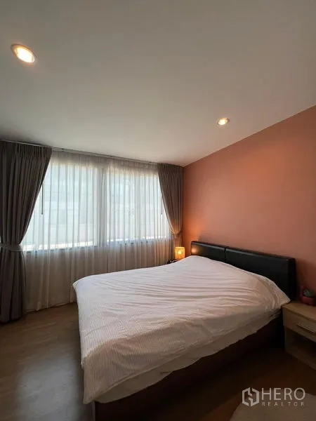 联排别墅 出租在Saphan Sung, Bangkok - 采光卧室，落地窗配窗帘，蜜桃色强调墙与双人床和床头灯。