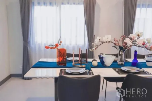 Detached House for rent in Bang Phli, Samut Prakan - Dining table set by double windows with grey curtains and floral decor.