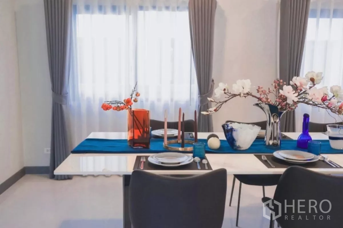 Detached House for rent in Bang Phli, Samut Prakan - Dining table set by double windows with grey curtains and floral decor.