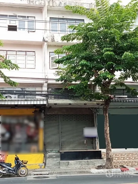 店屋 出租在Phra Khanong, Bangkok - 帕卡农街景中的多层店屋外立面，设金属卷闸门与行道树。