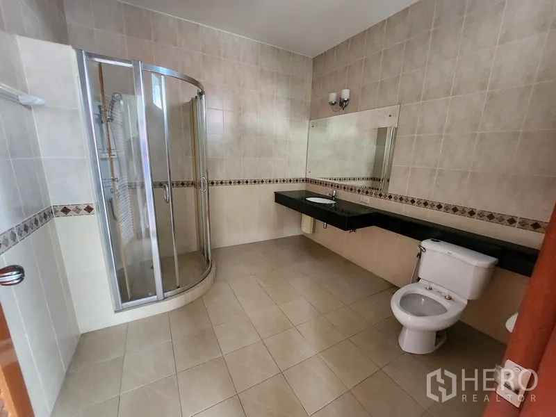 Detached House for rent in Prawet, Bangkok - Tiled bathroom with glass shower enclosure, long stone vanity and toilet.