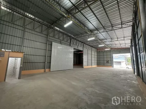 Warehouse for rent in Bueng Kum, Bangkok - Spacious warehouse interior with high steel truss ceiling, large sliding door, and a built-in restroom.
