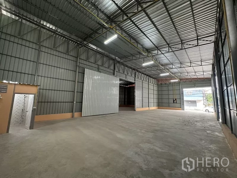 Warehouse for rent in Bueng Kum, Bangkok - Spacious warehouse interior with high steel truss ceiling, large sliding door, and a built-in restroom.