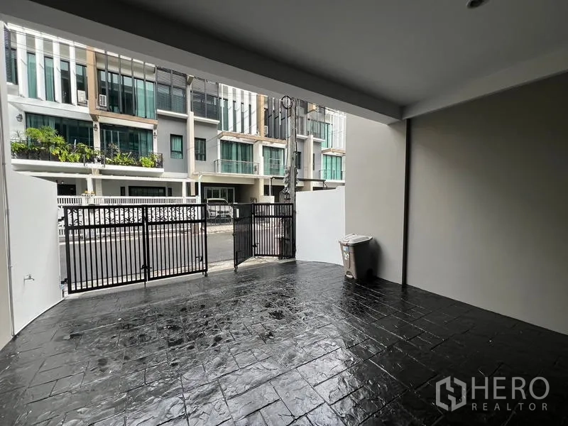 Townhouse for rent or sale in Khlong Toei, Bangkok - Covered carport with a black gate facing a quiet townhouse lane.