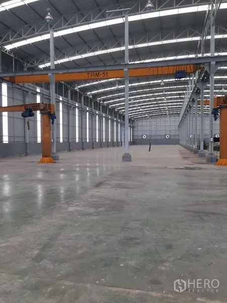 Factory for rent or sale in Samut Sakhon - High-roof warehouse interior with steel trusses and 5-ton overhead cranes along multiple bays.