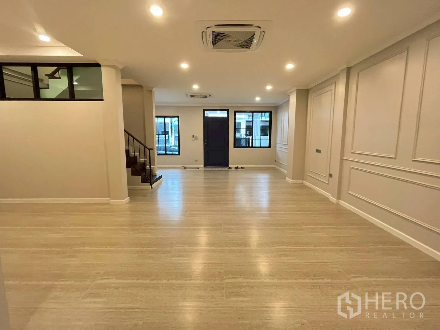 Townhouse for rent in Khlong Toei, Bangkok - Wide view of large living room with recessed lighting, paneled walls, and front door.