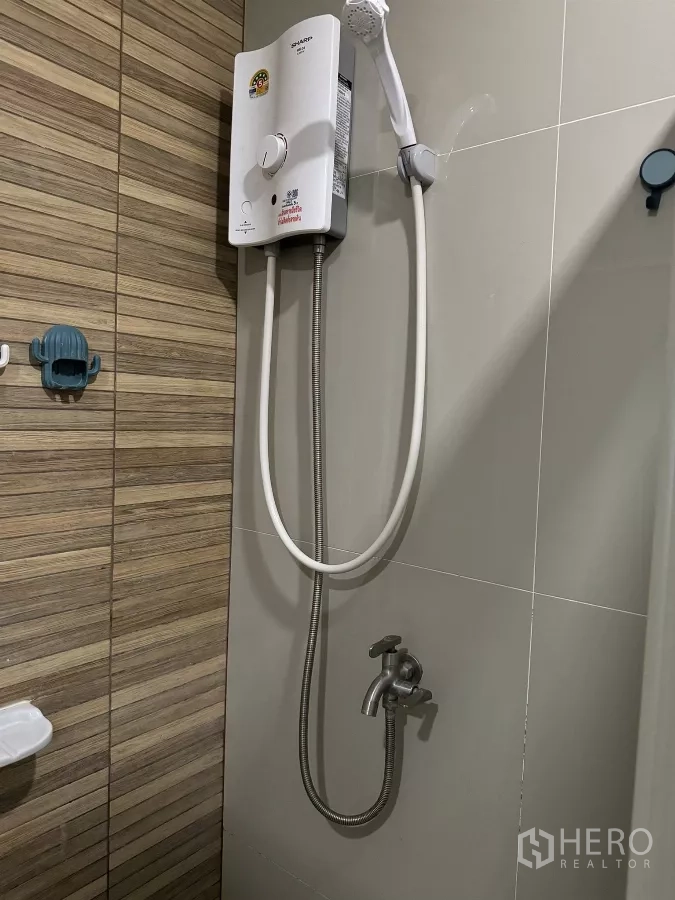 Townhouse for rent in Suan Luang, Bangkok - Bathroom shower area with instant water heater, handheld showerhead, and neutral wall tiles.