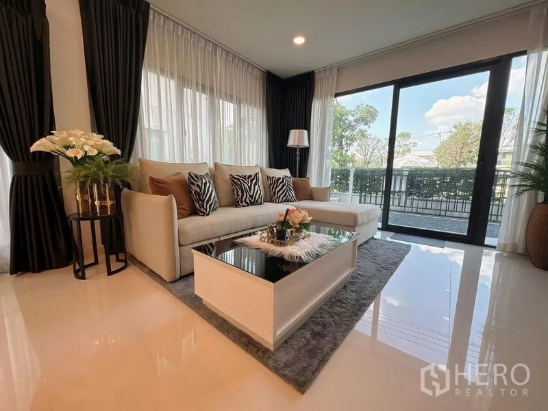 Detached House for rent or sale in Bang Phli, Samut Prakan - Light-filled living room with L-shaped sofa, coffee table and wide sliding doors to the garden.