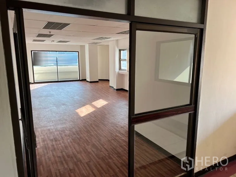 Office Space for rent in Pathum Wan, Bangkok - View through a glass entry partition into a spacious office area with natural light and wood-style floors.