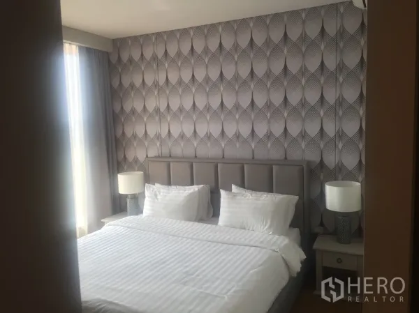 Condominium for rent in Khlong Toei, Bangkok - Cozy bedroom with patterned feature wall, large bed, bedside tables, and soft daylight from the window.