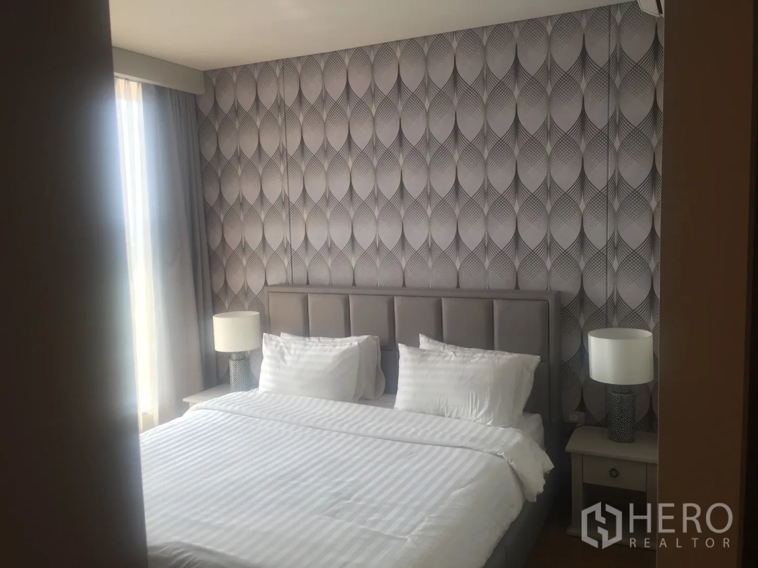 Condominium for rent in Khlong Toei, Bangkok - Cozy bedroom with patterned feature wall, large bed, bedside tables, and soft daylight from the window.