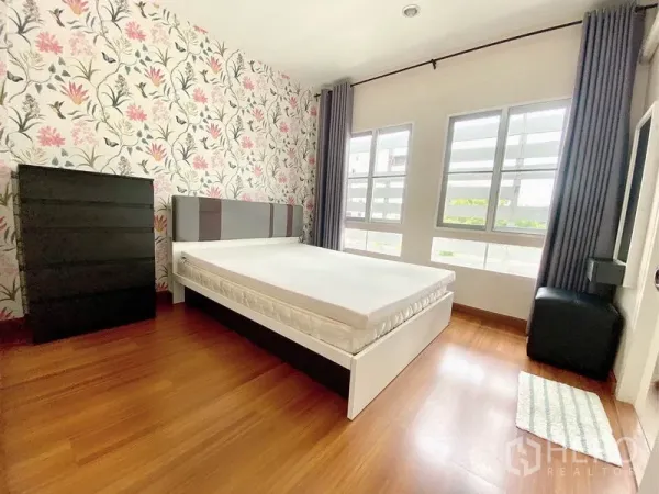 Townhouse for rent in Prawet, Bangkok - Sunlit secondary bedroom with floral wallpaper, bed, dresser and double windows.
