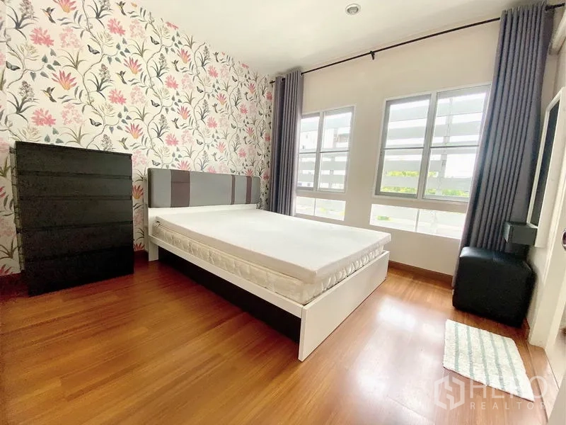 Townhouse for rent in Prawet, Bangkok - Sunlit secondary bedroom with floral wallpaper, bed, dresser and double windows.