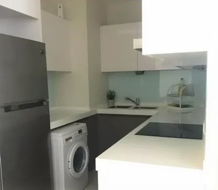 Condominium for rent in Pathum Wan, Bangkok - Compact U‑shaped kitchen with white cabinetry, cooktop, fridge and washing machine.