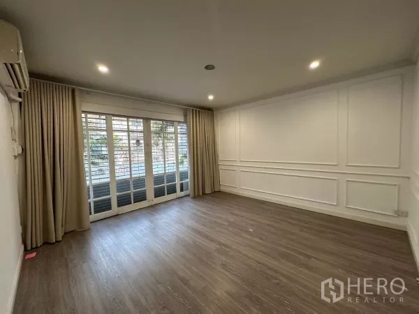 Townhouse for rent in Watthana, Bangkok - Bright living room with wood floors, wall paneling and sliding glass doors with curtains.