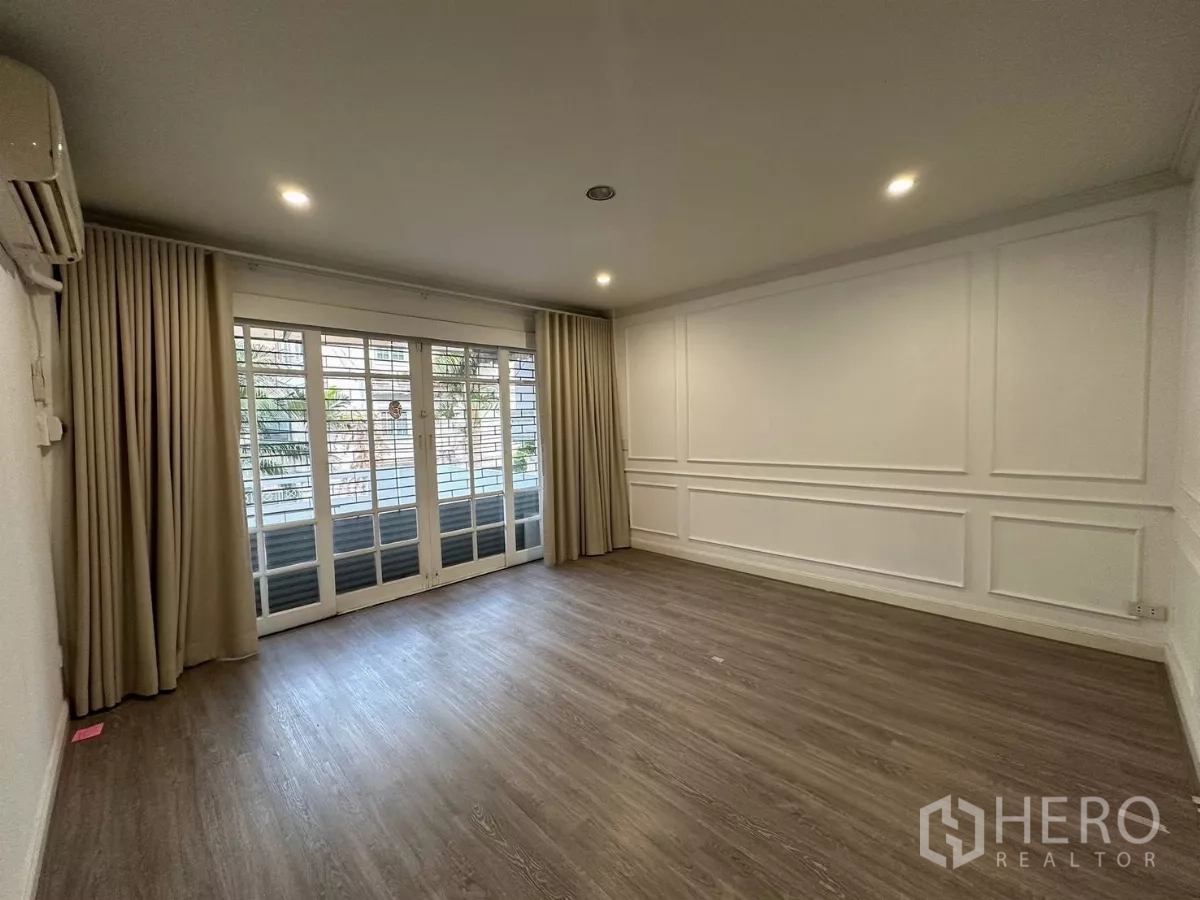 Townhouse for rent in Watthana, Bangkok - Bright living room with wood floors, wall paneling and sliding glass doors with curtains.
