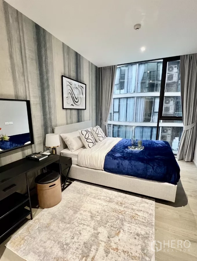 Condominium for rent in Khlong Toei, Bangkok - Spacious bedroom with area rug and tall windows.