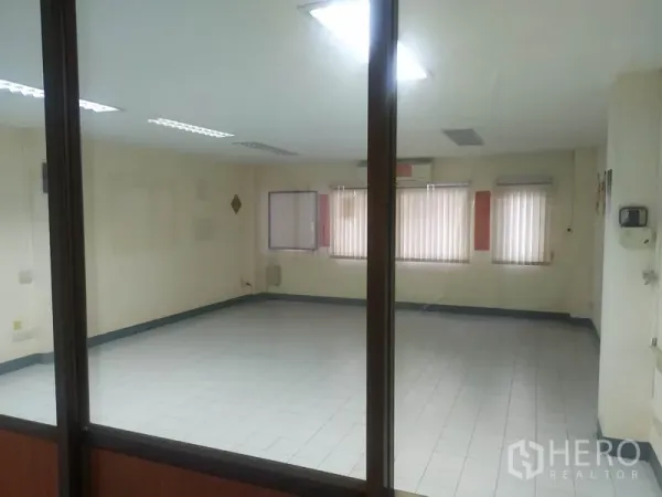 Home Office for rent in Yan Nawa, Bangkok - Large empty office room seen through a glass partition with windows and blinds.