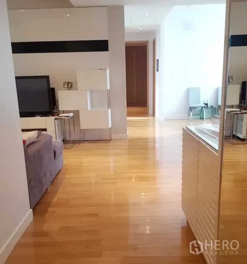 Condominium for rent in Khlong Toei, Bangkok - Bright open-plan living area with light wood flooring, TV console and hallway view.
