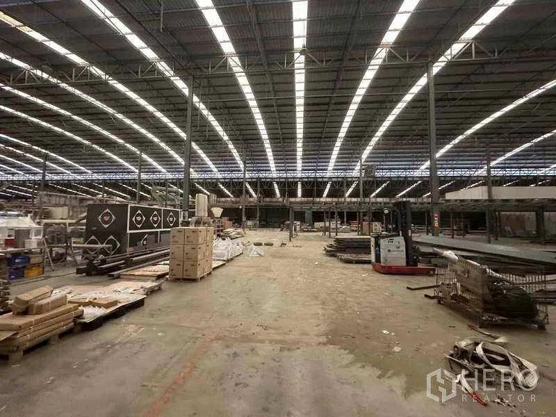 Factory for rent in Pathum Thani - Central hall with high‑span roof, open floor and materials staged for processing.