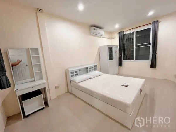 Townhouse for rent in Huai Khwang, Bangkok - Bright furnished bedroom with white bed, vanity, wardrobe, air conditioner and large window.