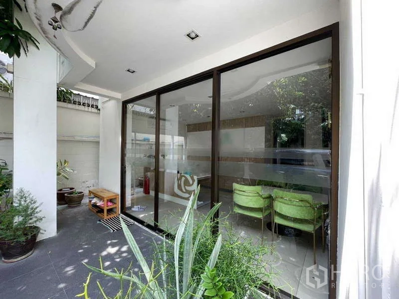 Home Office for rent in Watthana, Bangkok - Covered patio with floor-to-ceiling glass wall and surrounding plants.