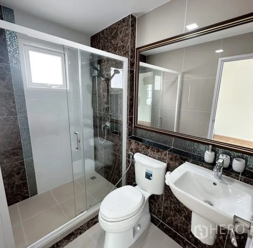 Detached House for rent in Mueang Samut Prakan, Samut Prakan - Contemporary bathroom featuring a large mirror and sliding glass shower with marble-effect tiles.