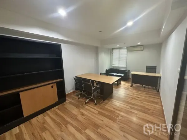 Office Space for rent in Khlong Toei, Bangkok - Private office with desks, black shelving, sofa seating, and window blinds on wood floors.
