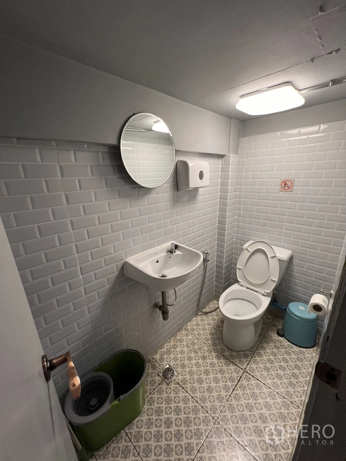 Shophouse for rent or sale in Watthana, Bangkok - Restroom with subway-tile walls, round mirror and patterned floor.