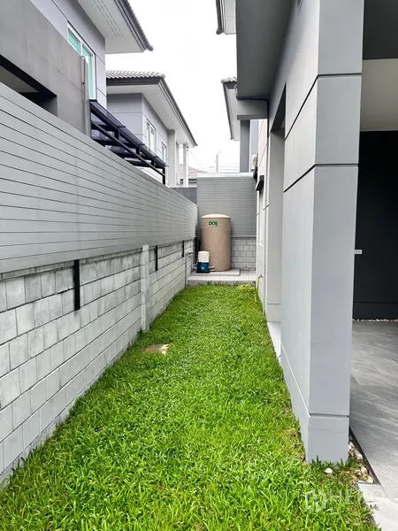 Detached House for sale in Prawet, Bangkok - Narrow side yard with green lawn, water tank and paved path along the house.