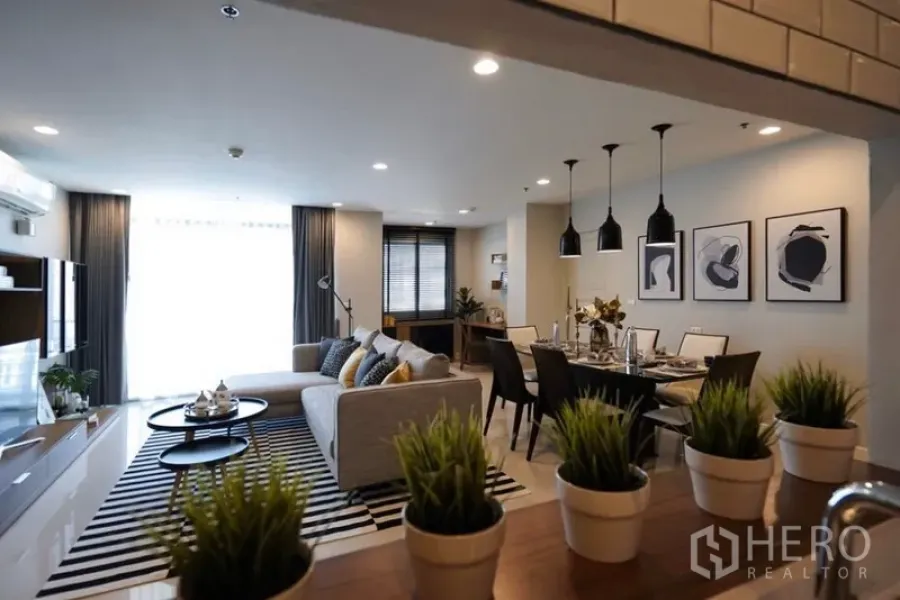 Condominium for rent in Watthana, Bangkok - Open-plan living and dining area with gray sofa, striped rug, pendant lights, and set dining table.