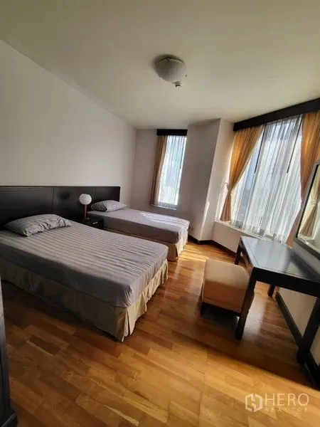 Condominium for rent in Pathum Wan, Bangkok - Bright bedroom with two single beds, desk and corner windows with curtains.