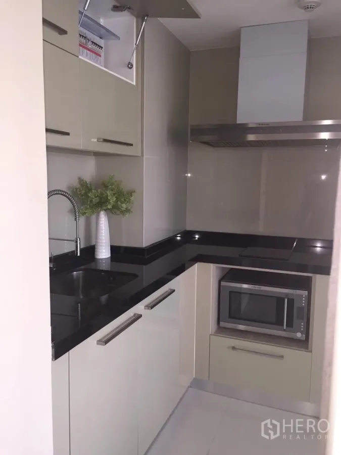 Condominium for rent in Khlong Toei, Bangkok - Compact U-shaped kitchen with black granite countertops, built-in microwave, cooktop and hood.