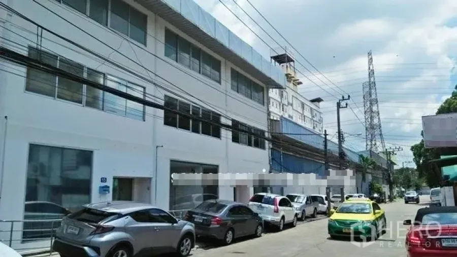 Warehouse for rent in Suan Luang, Bangkok - Street view of a white two-storey warehouse and office facade with parking and several cars.