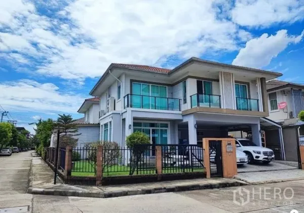 Detached House for sale in Suan Luang, Bangkok - Two-storey detached house in Suan Luang, Bangkok with balconies, gated fence, lawn and covered parking under a blue sky.