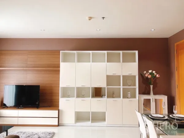 Condominium for rent in Khlong Toei, Bangkok - Built-in shelving beside the TV console and a dining area in an open-plan space.