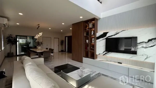 Detached House for rent in Bang Phli, Samut Prakan - Open-plan living and dining room with marble TV wall and wood shelving.
