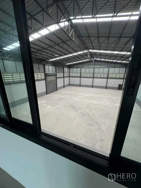 Factory for sale in Samut Sakhon - Interior view from office window into high-bay warehouse with steel roof structure.