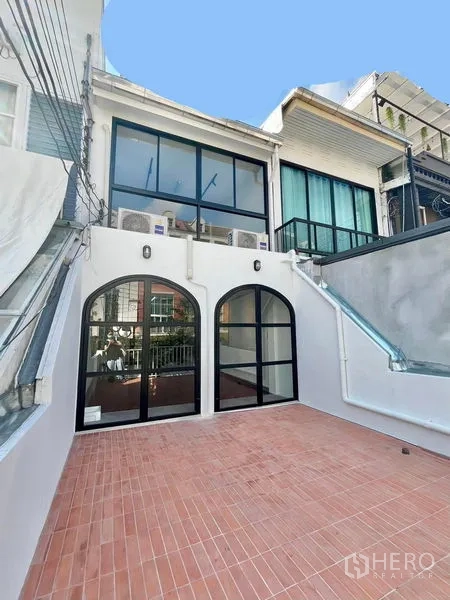 Home Office for rent in Khlong Toei, Bangkok - Spacious rear terrace with terracotta tiles, arched black-framed glass doors and side steps.