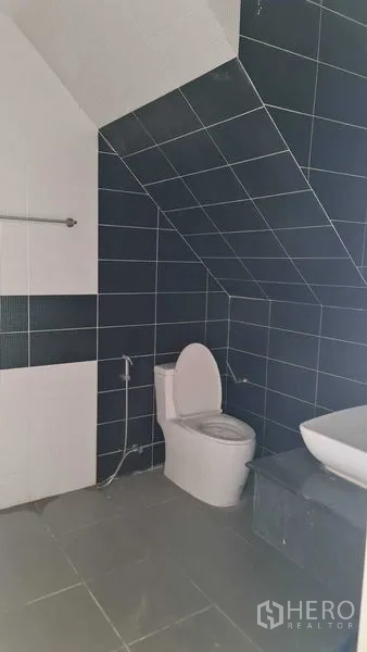 Townhouse for  in Lam Luk Ka, Pathum Thani - Toilet and sink under a sloped ceiling with dark tiles.