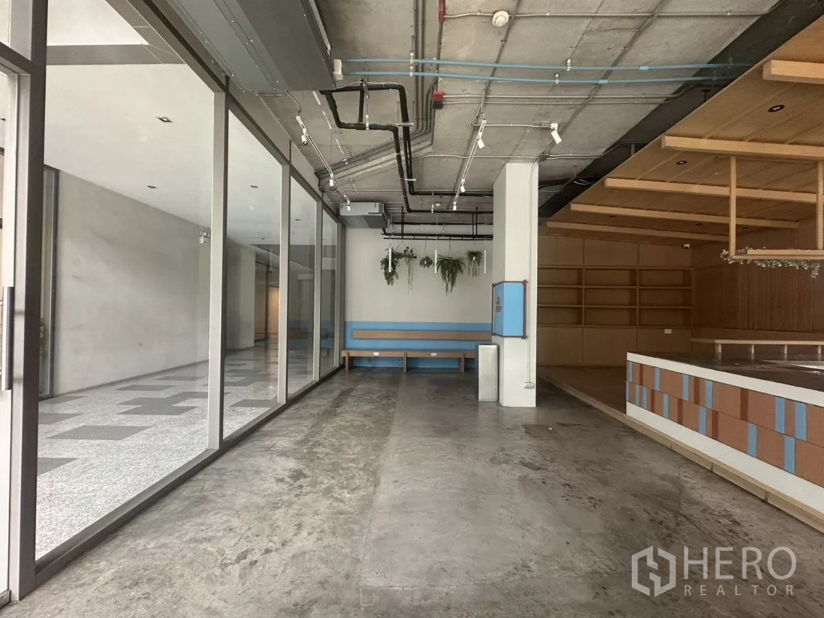Retail Space for rent - Wide view along the glass storefront showing exposed ceiling, track lights, and a raised counter platform.