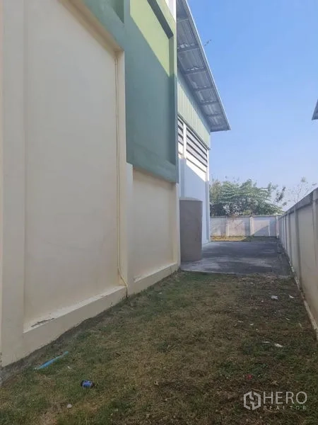Factory for rent or sale in Lam Luk Ka, Pathum Thani - Side passage along the building with grass strip and concrete path.