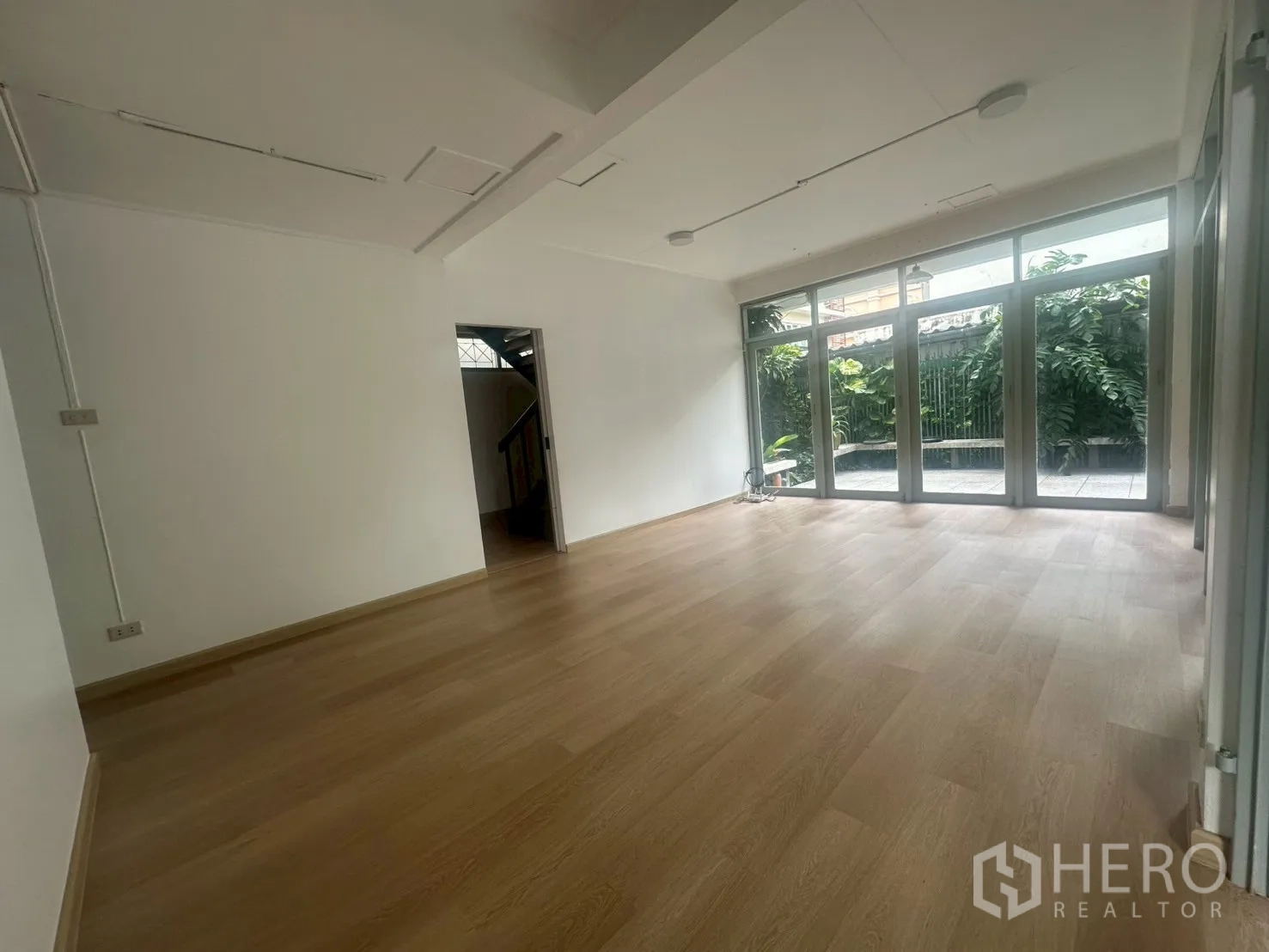 Detached House for rent in Watthana, Bangkok - Spacious open-plan room with garden views through large windows and light timber flooring.